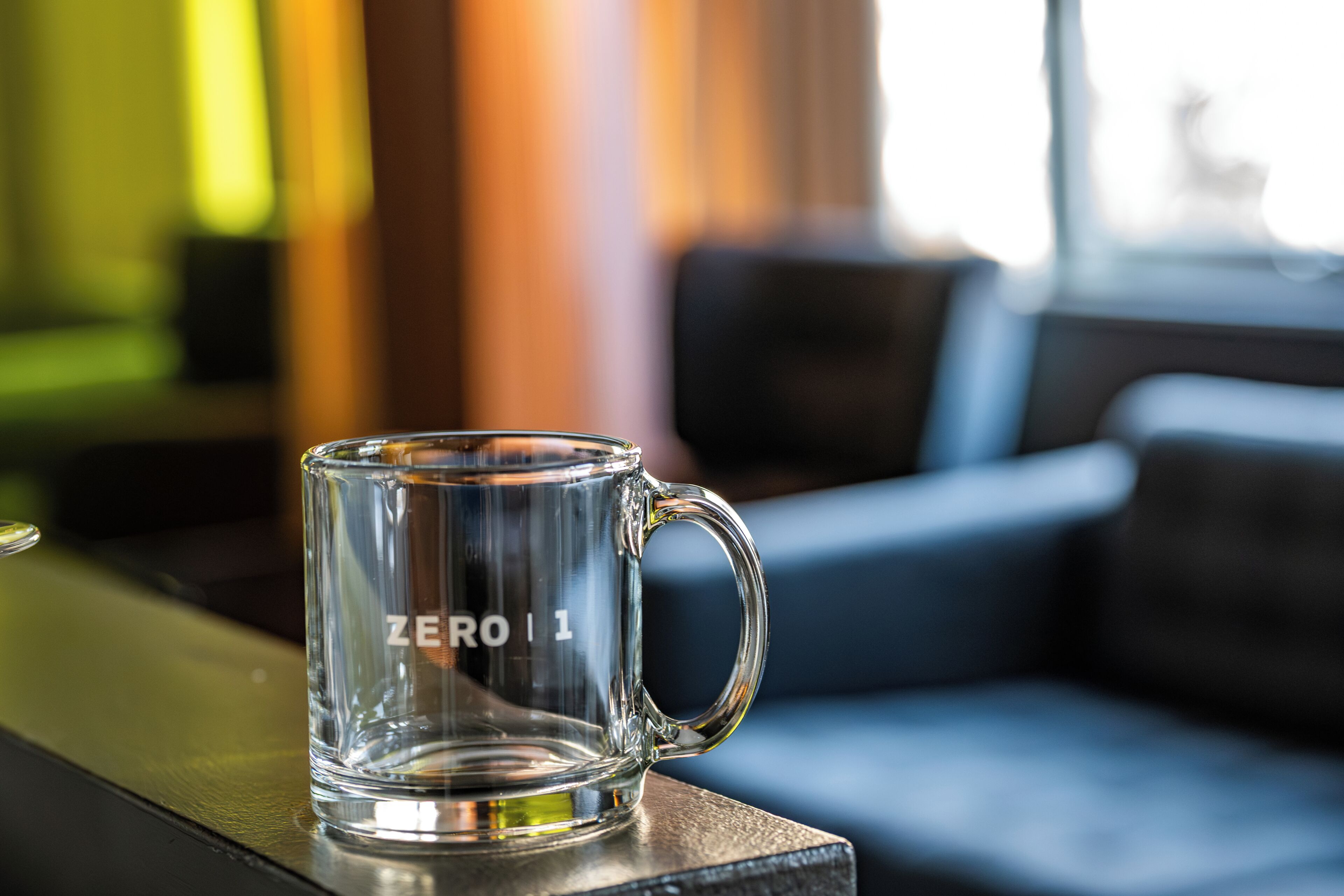 Une tasse en verre transparent portant l’inscription « ZERO 1 » et posée sur une surface en bois.