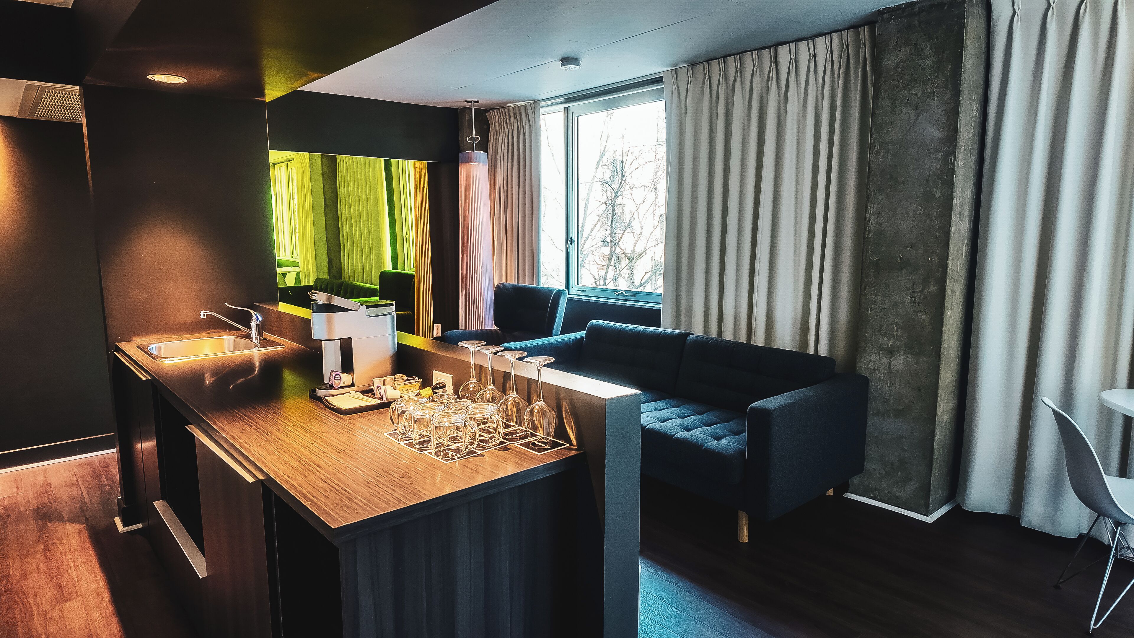 Une chambre moderne avec un bureau en bois, un canapé, une fenêtre avec des rideaux et une vue sur les arbres.