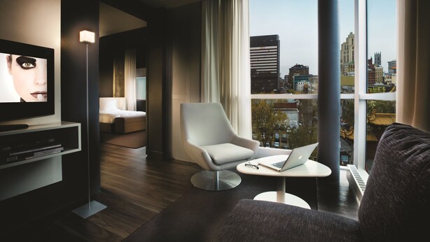 Un salon moderne avec vue sur la ville, un téléviseur à écran plat, un fauteuil confortable et une petite table sur laquelle se trouve un ordinateur portable.