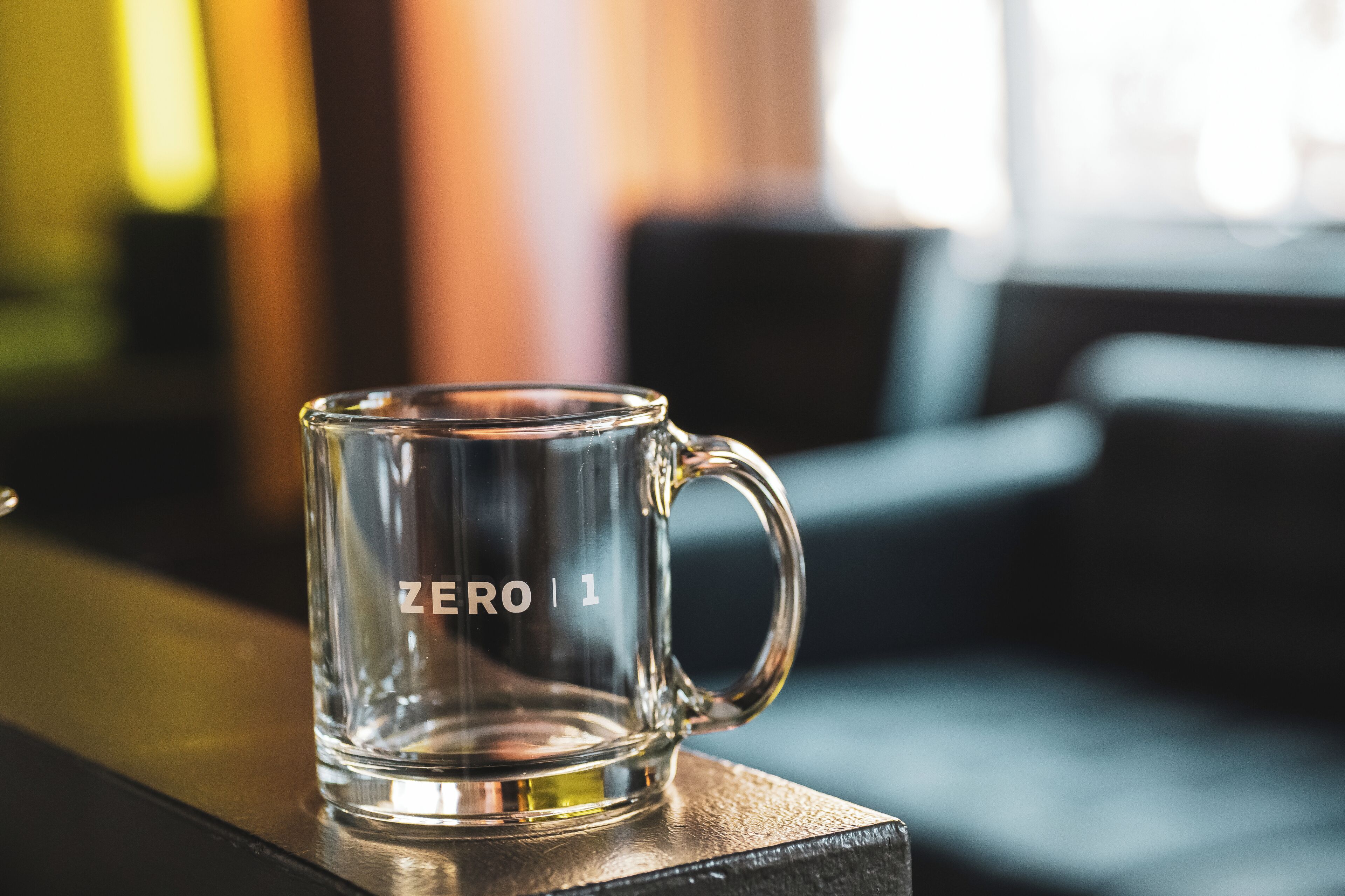 Une tasse en verre transparent portant l’inscription « ZERO | 1 » et posée sur une surface en bois.