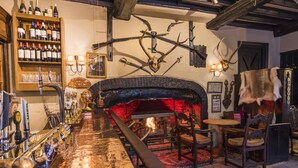 A bar area with a fireplace, wooden shelves with bottles, and a rustic decor including antlers and a fur coat. - Luttrell Arms Hotel (Minehead)
