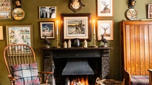 A cozy room with a fireplace, framed pictures, and a wooden chair. - Luttrell Arms Hotel (Minehead)