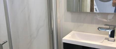 A bathroom with a glass-enclosed shower, a white sink with a black cabinet, and a mirror with a round frame.