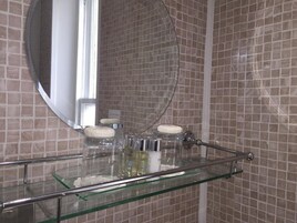 Un baño con repisas de vidrio que sostienen artículos de tocador, un espejo redondo y una pared con azulejos.