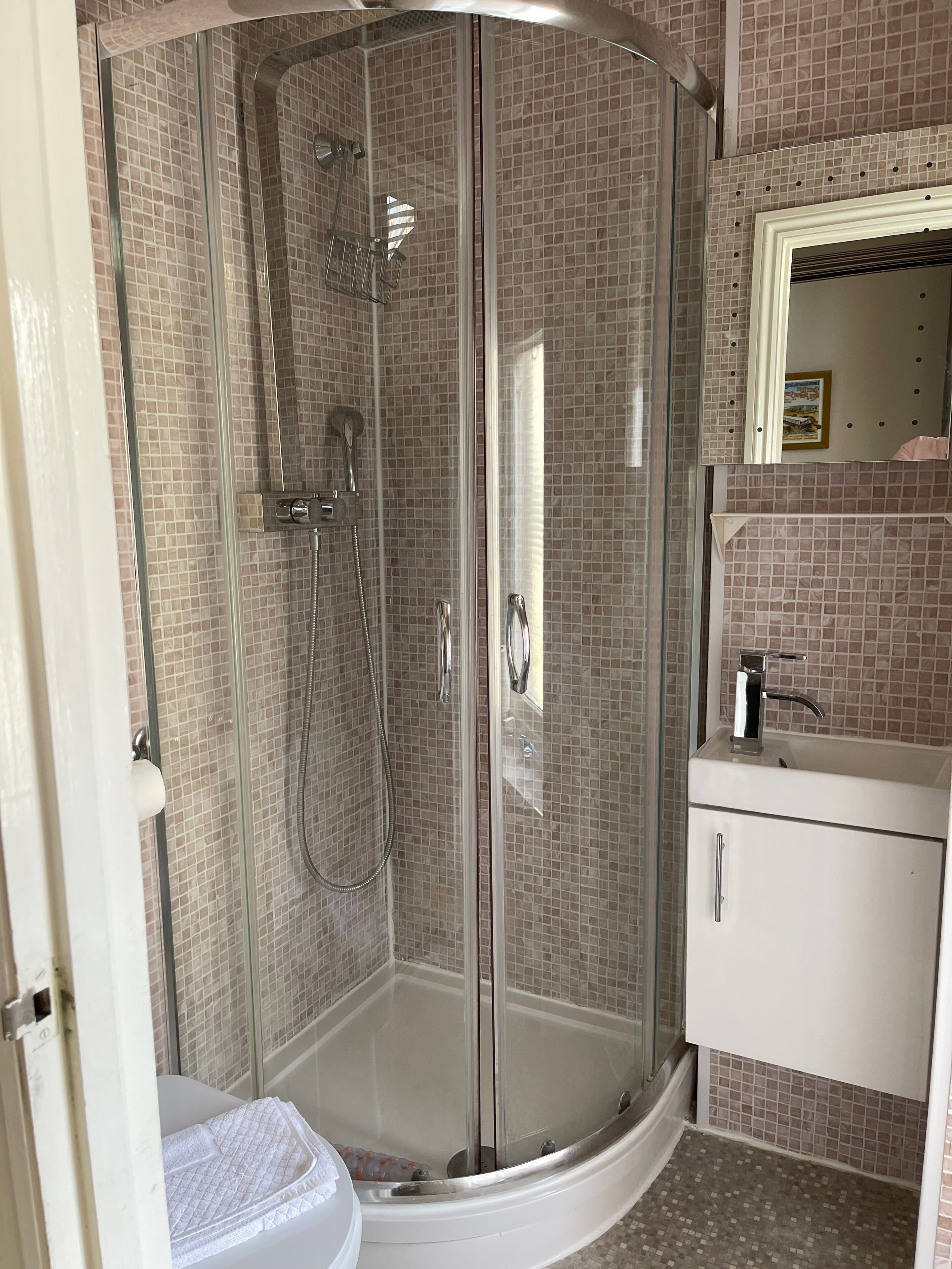 Ducha en esquina con puertas de vidrio, lavamanos blanco y pared con azulejos.