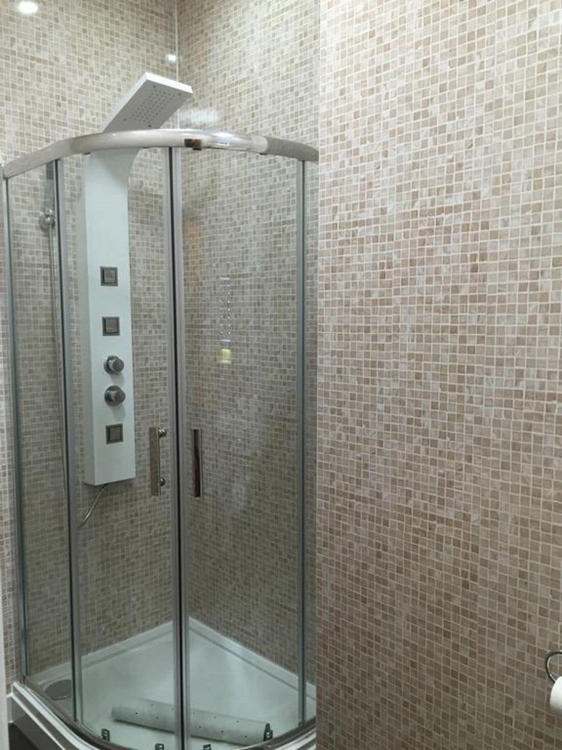 Un vestuario de ducha con paredes de azulejos, panel de control y un toallero visible.