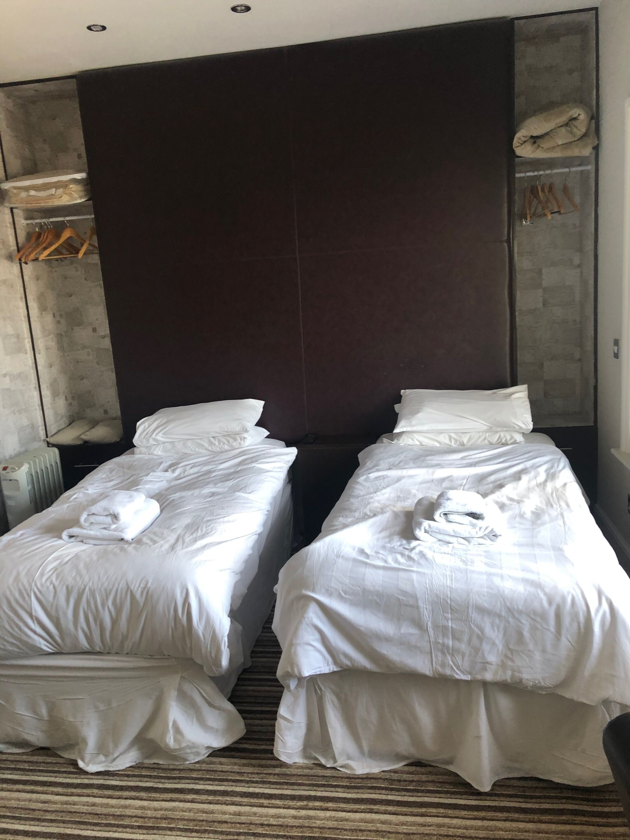 Quarto de hotel com duas camas de solteiro, cada uma com toalhas brancas dobradas, cabeceira escura e carpete listrado.