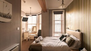 Quarto bem arrumado com cama, mesa de cabeceira e escrivaninha com cadeira.