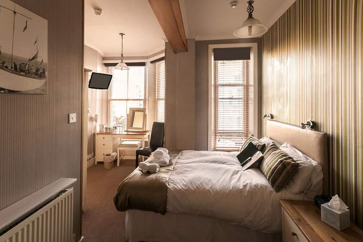 A neatly arranged bedroom with a bed, bedside table, and a desk with a chair.
