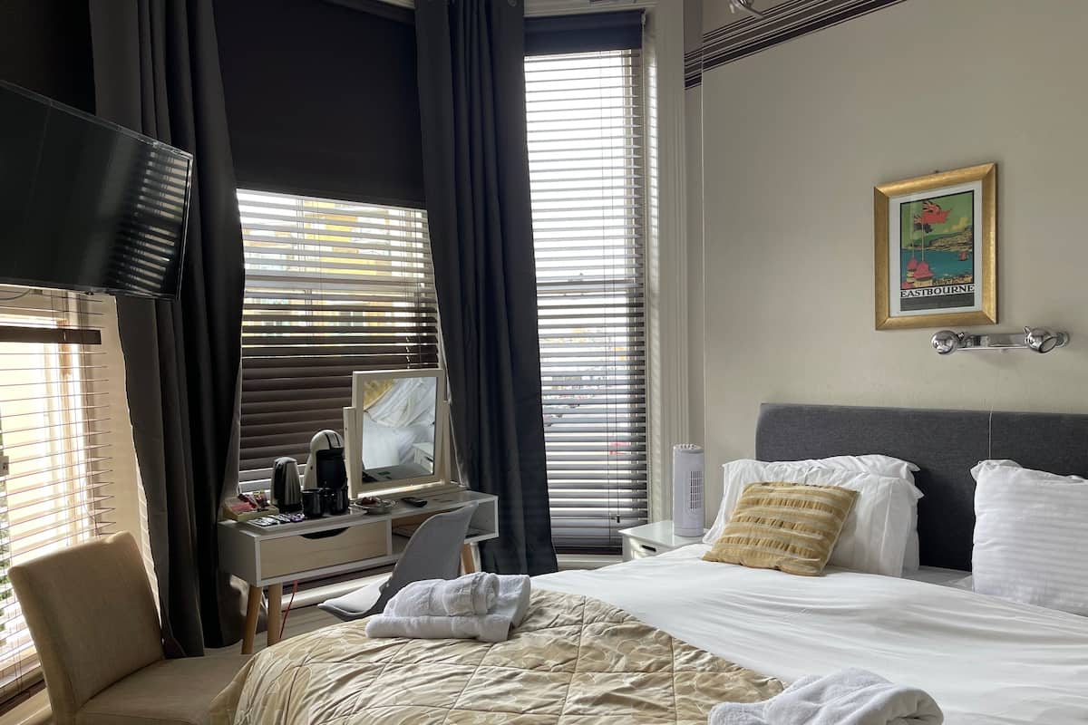 A hotel room with a bed, a desk with a computer, a chair, and a window with blinds.