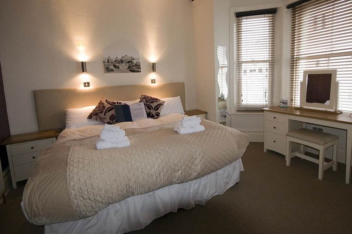 A neatly arranged bedroom with a large bed, bedside tables, a desk, and a window with blinds.