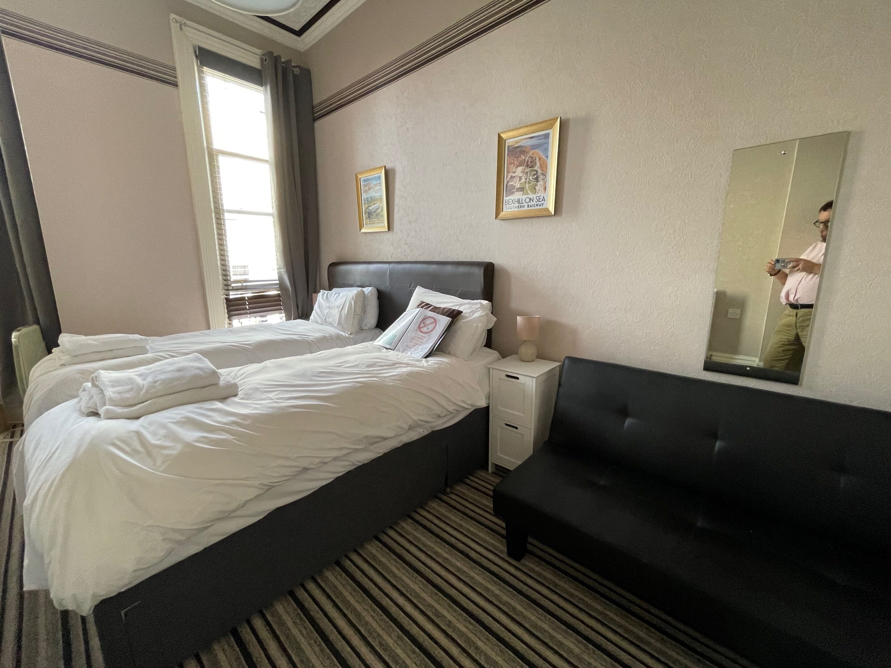 A hotel room with a large bed, a bedside table, a black sofa, and a mirror.