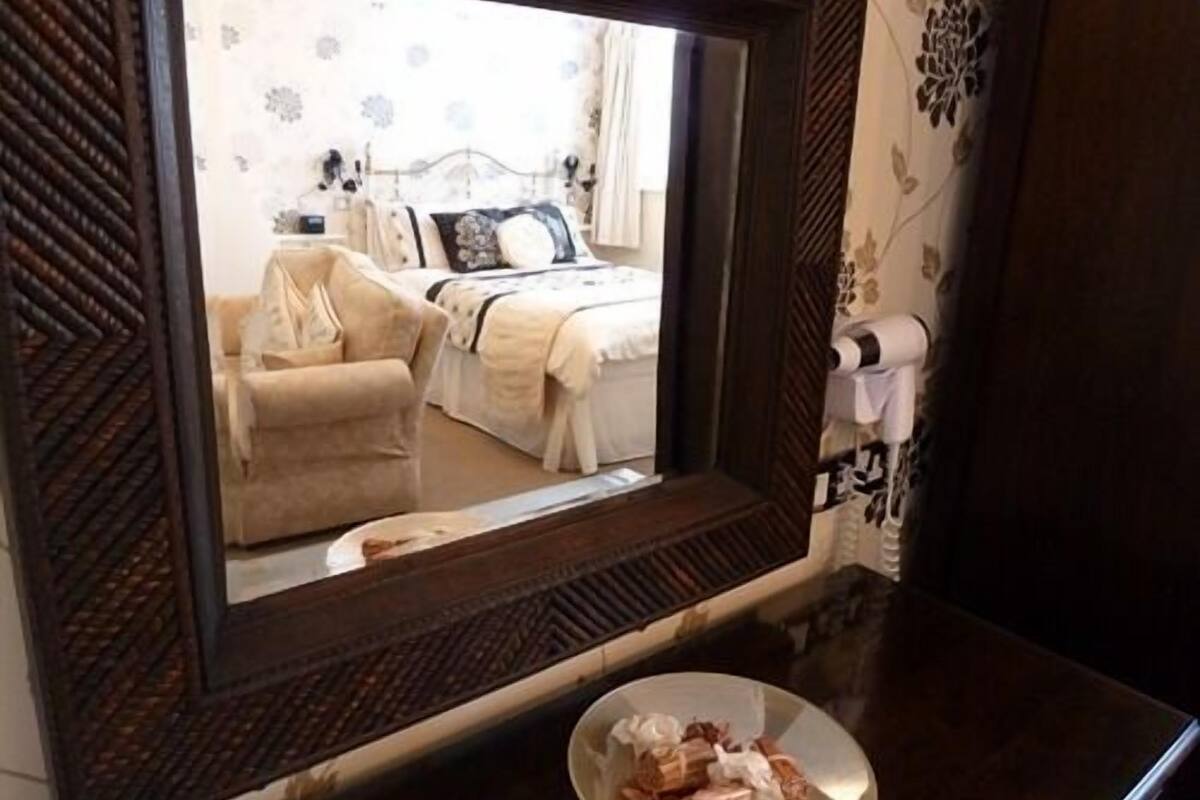 Een spiegel toont een slaapkamer met een bed, een stoel en een nachtkastje met een bord eten.