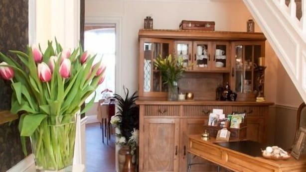 Un armario de madera con puertas de cristal, un jarrón con tulipanes rosas y una mesa de madera con un periódico.
