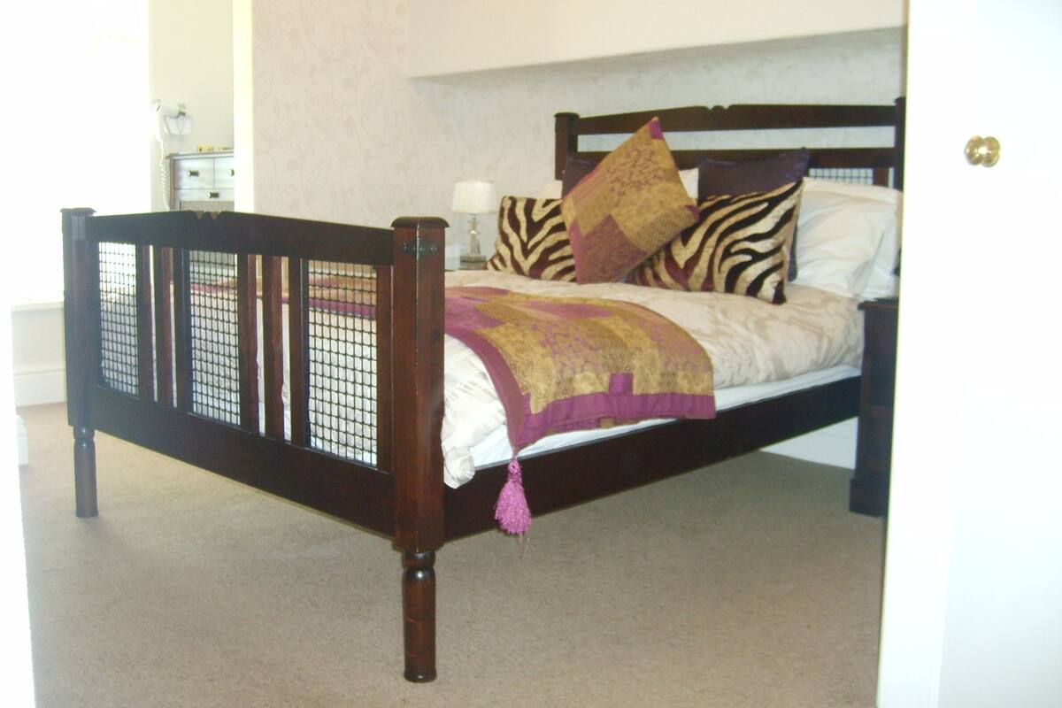 Een slaapkamer met een houten bedframe, een bed met een decoratief sprei en een nachtkastje met een lamp.