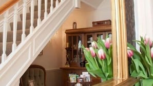 Una escalera con barandilla blanca, un mueble de madera con puertas de cristal y un jarrón con tulipanes rosas.