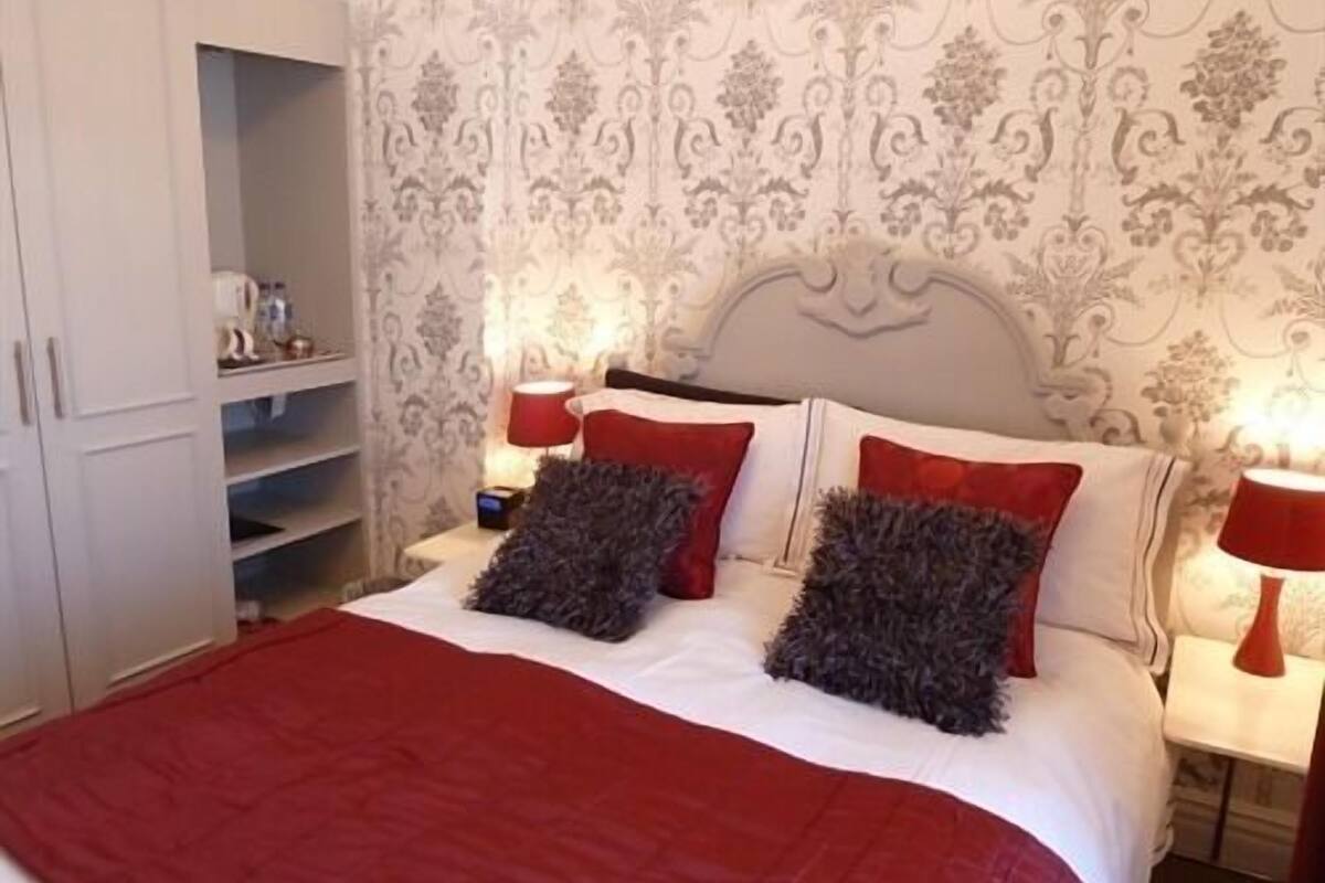 Een slaapkamer met een bed, twee nachtkastjes, een kledingkast en behang met een patroon.