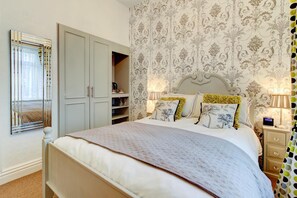 A bedroom with a bed, bedside lamps, a nightstand, a mirror, and a wardrobe. - North Crest (Blackpool)