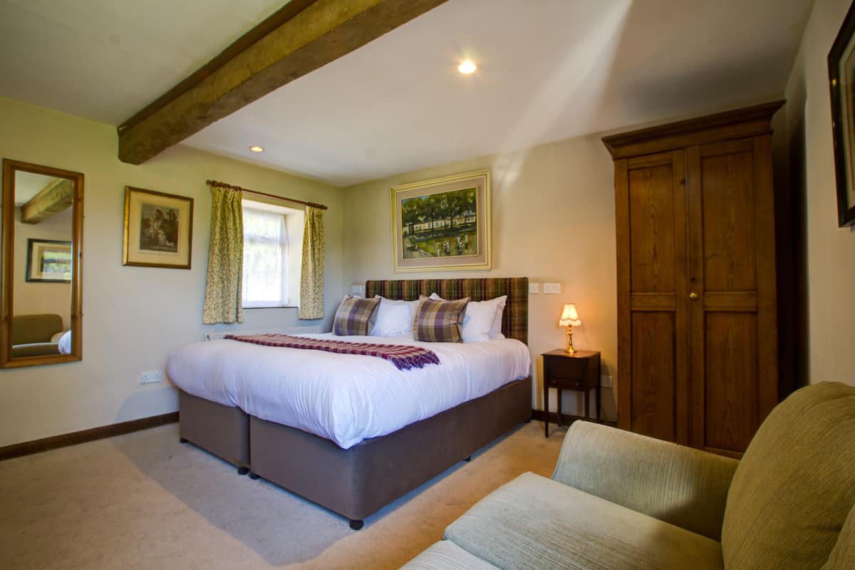 A bedroom with a large bed, a wooden wardrobe, a bedside table with a lamp, and a window with curtains.