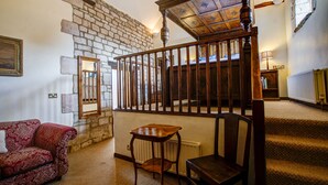 A staircase with wooden railings, a red patterned sofa, a small wooden table, and a chair. - The Moonraker Hotel (Trowbridge)