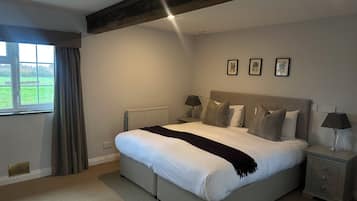 Un dormitorio con una cama grande, dos mesitas de noche, un radiador y una ventana con cortinas.