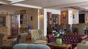A cozy living room with a red leather sofa, patterned armchairs, and a coffee table. A bar area is visible in the background with a sign labeled "BAR". - The Moonraker Hotel (Trowbridge)