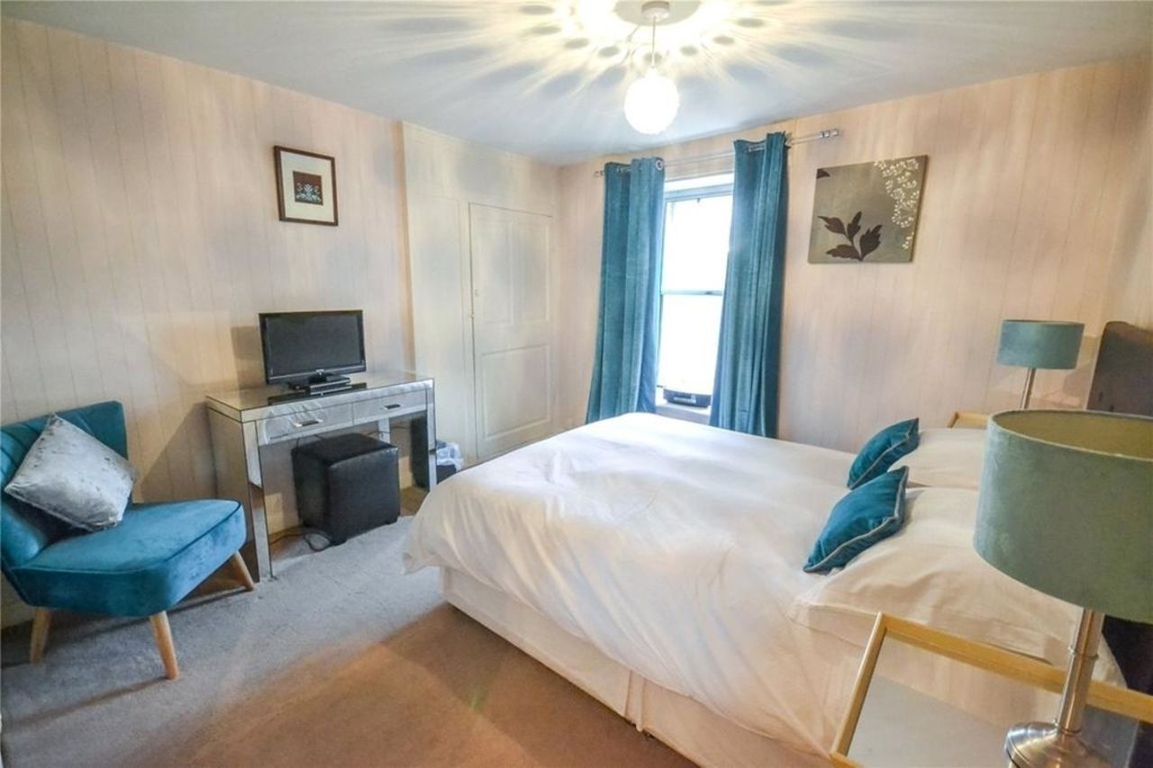 A hotel room with a bed, a desk with a television, a chair, a lamp, and a window with curtains.