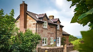 Une maison en pierre avec une cheminée en briques, des volets blancs et un mur en pierre.