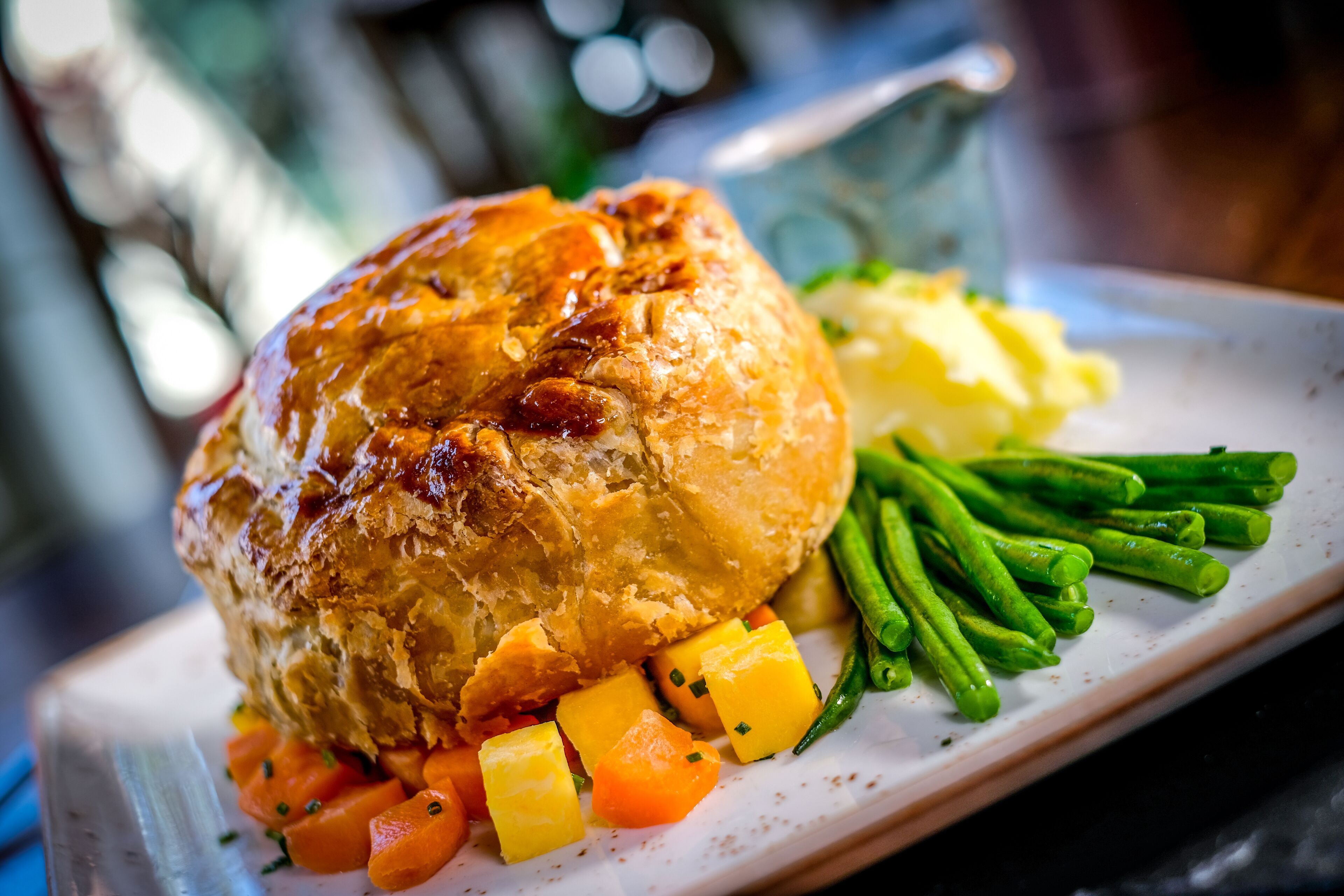 A plate with a pastry, green beans, and diced vegetables.