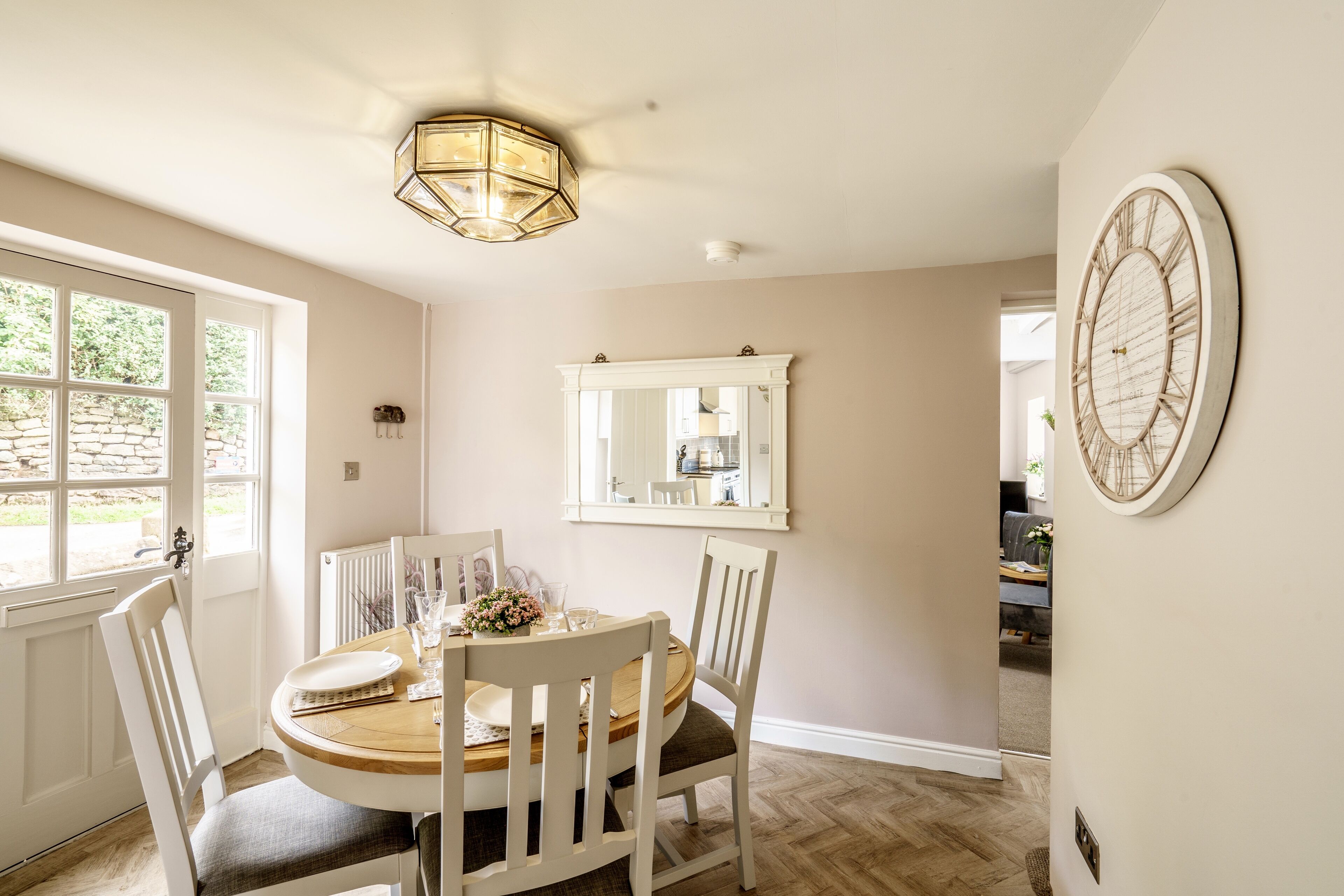 A dining area with a round table, white chairs, a chandelier, a mirror, and a wall clock.