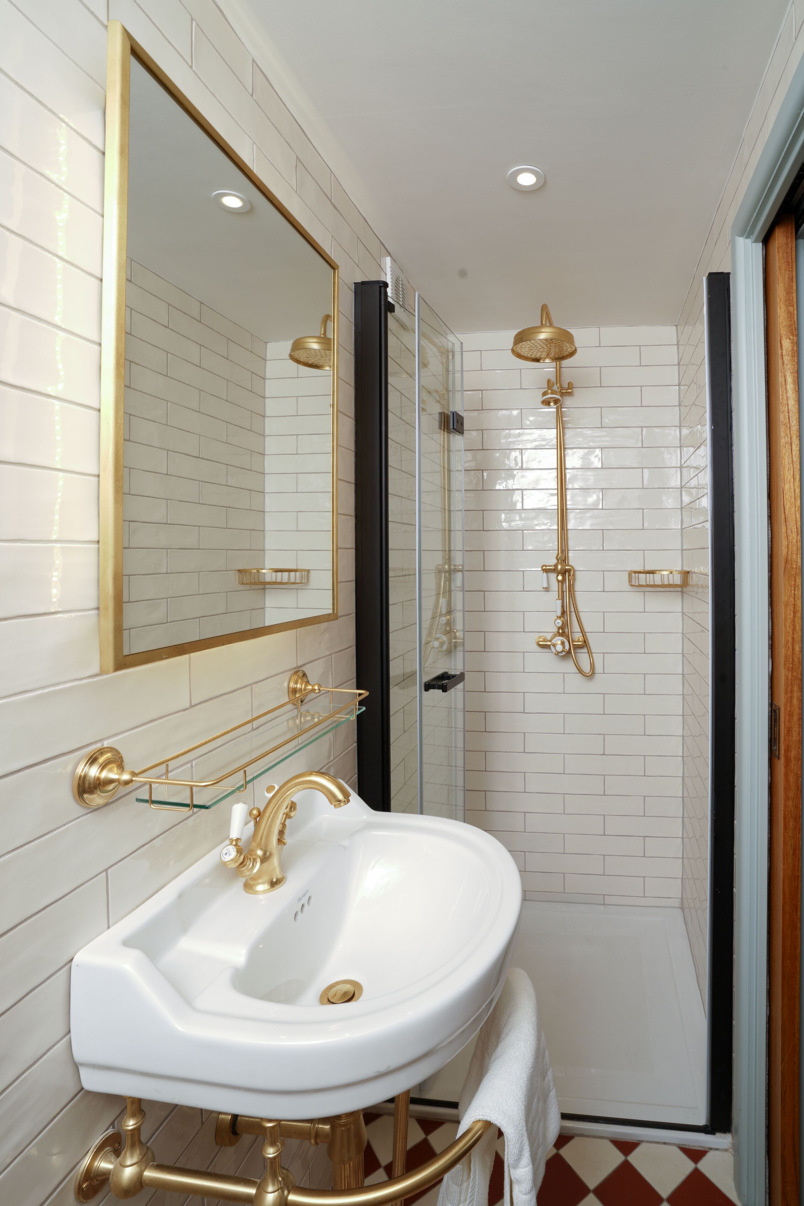 Een badkamer met een wit wastafelmeubel, gouden details en een douchecabine van glas.