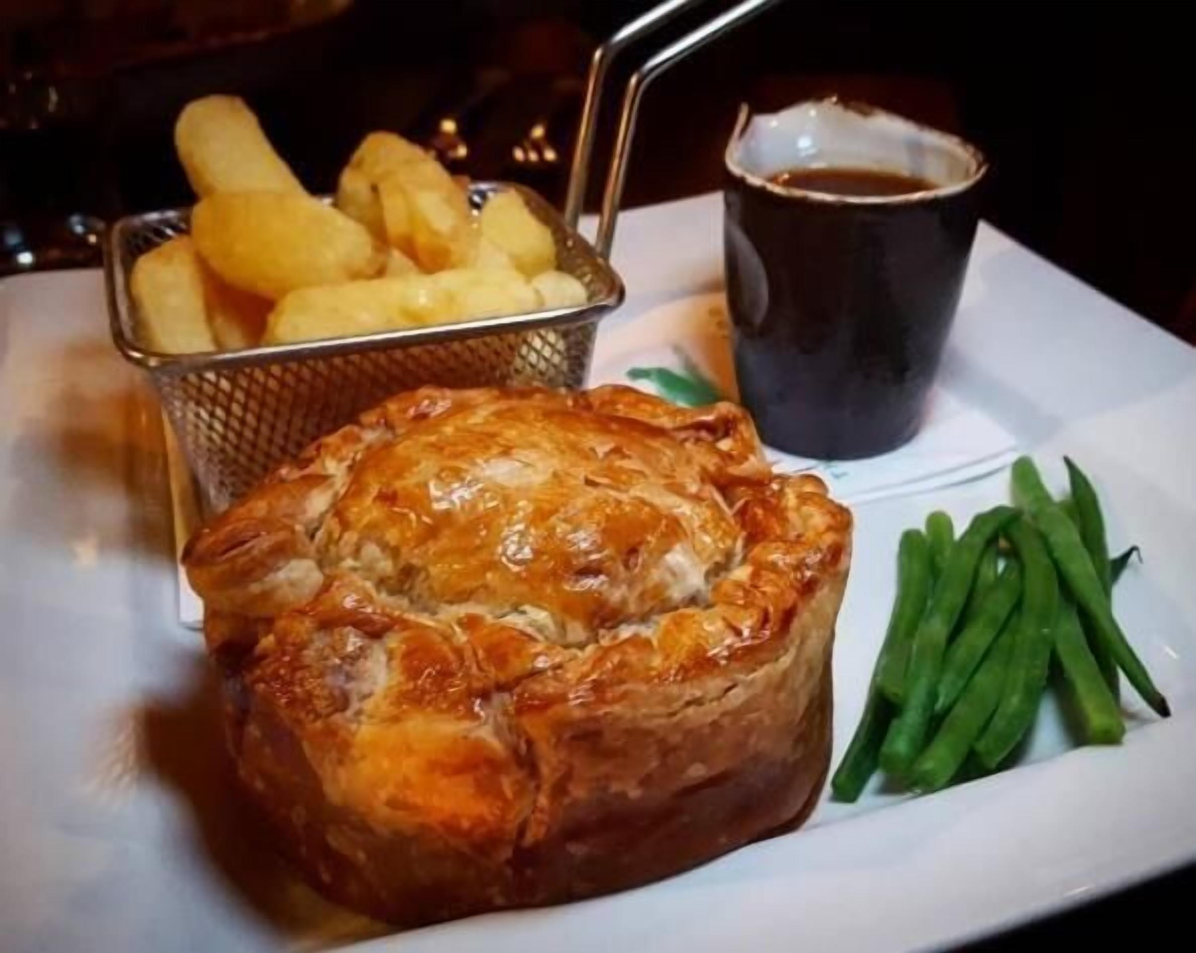 A plate with a meat pie, green beans, and a basket of fries.