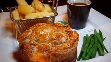 A plate with a meat pie, green beans, and a basket of fries.