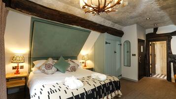 A bedroom with a large bed, two bedside tables with lamps, a chandelier, and a door leading to another room.