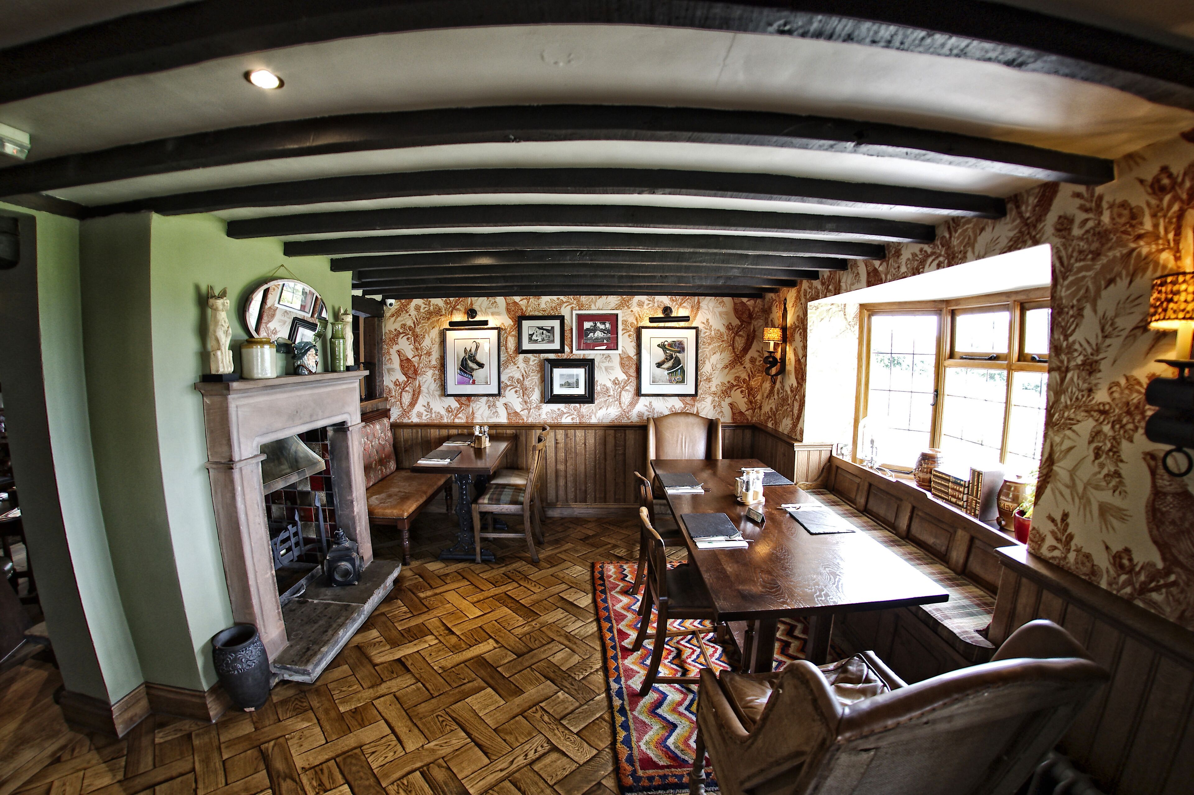 A traditional inn with a wooden interior, a fireplace, and a dining area with benches and tables.