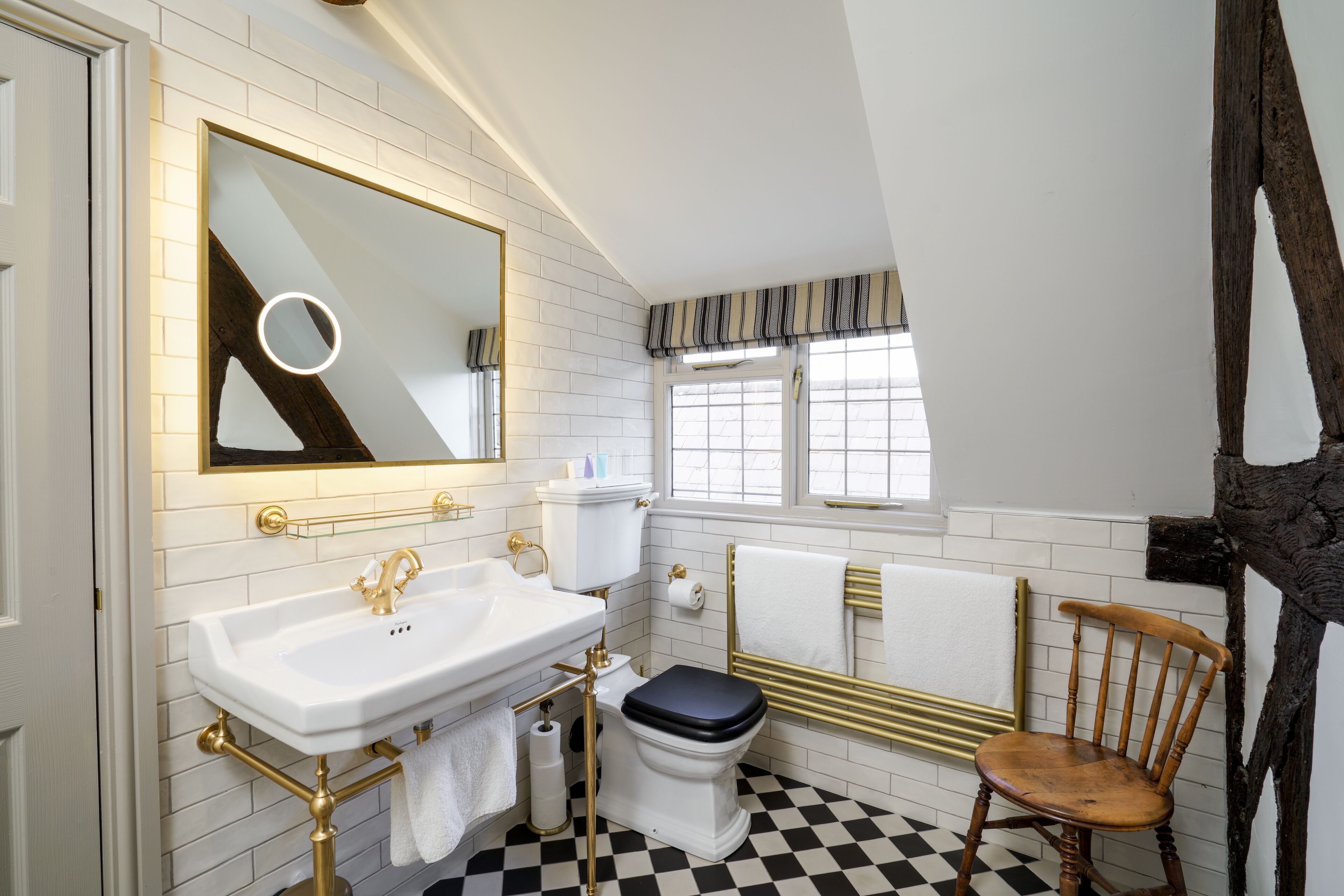 Un baño con lavamanos blanco, inodoro y una silla de madera.