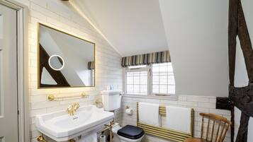 Un baño con lavamanos blanco, inodoro y una silla de madera.