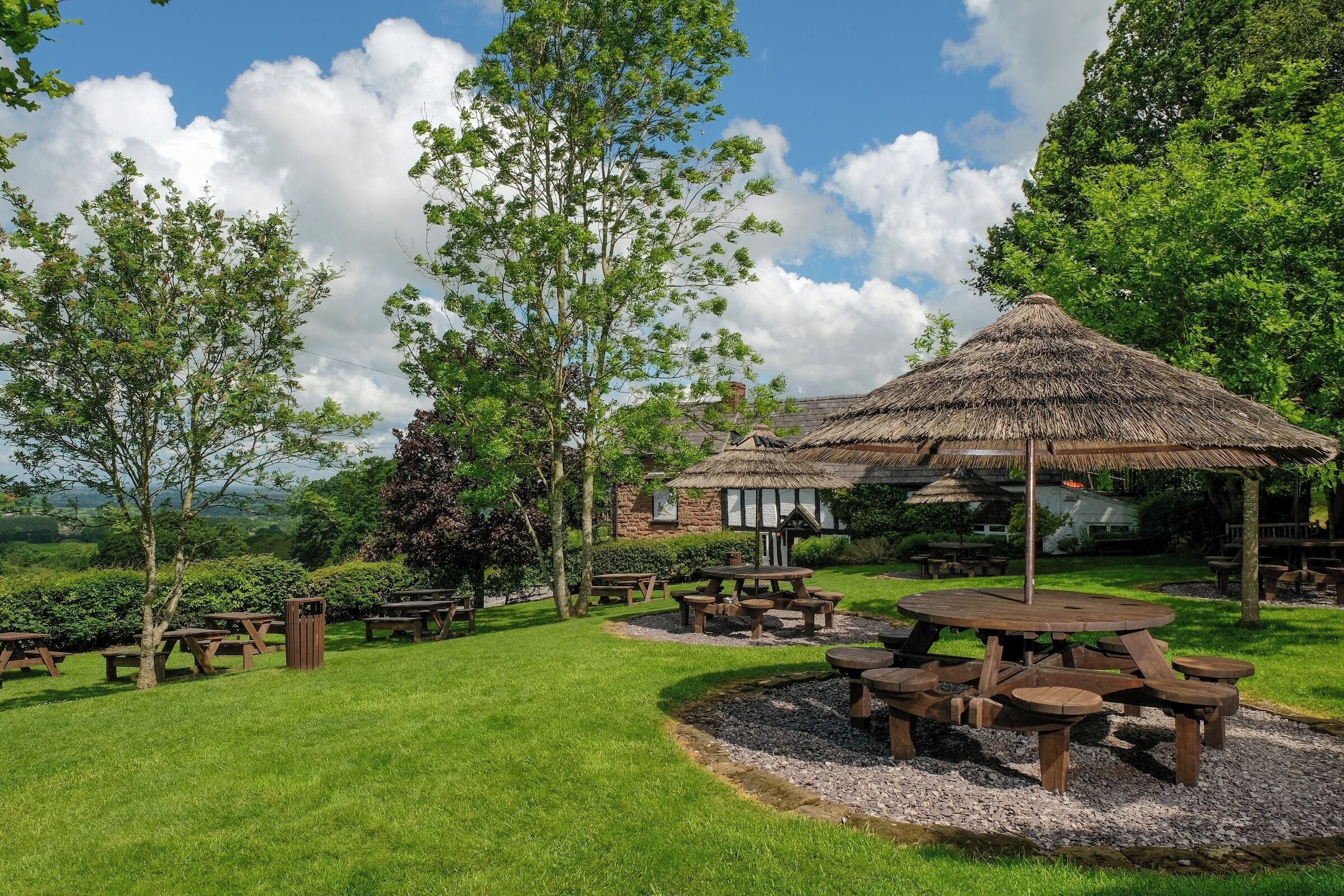 Un jardín con mesas de picnic y una estructura de techo de paja.