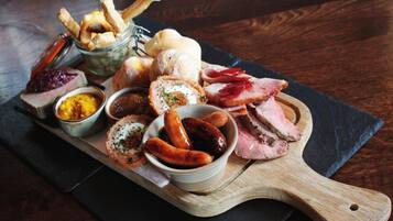 A wooden board with various food items including sausages, bread, and a pastry.