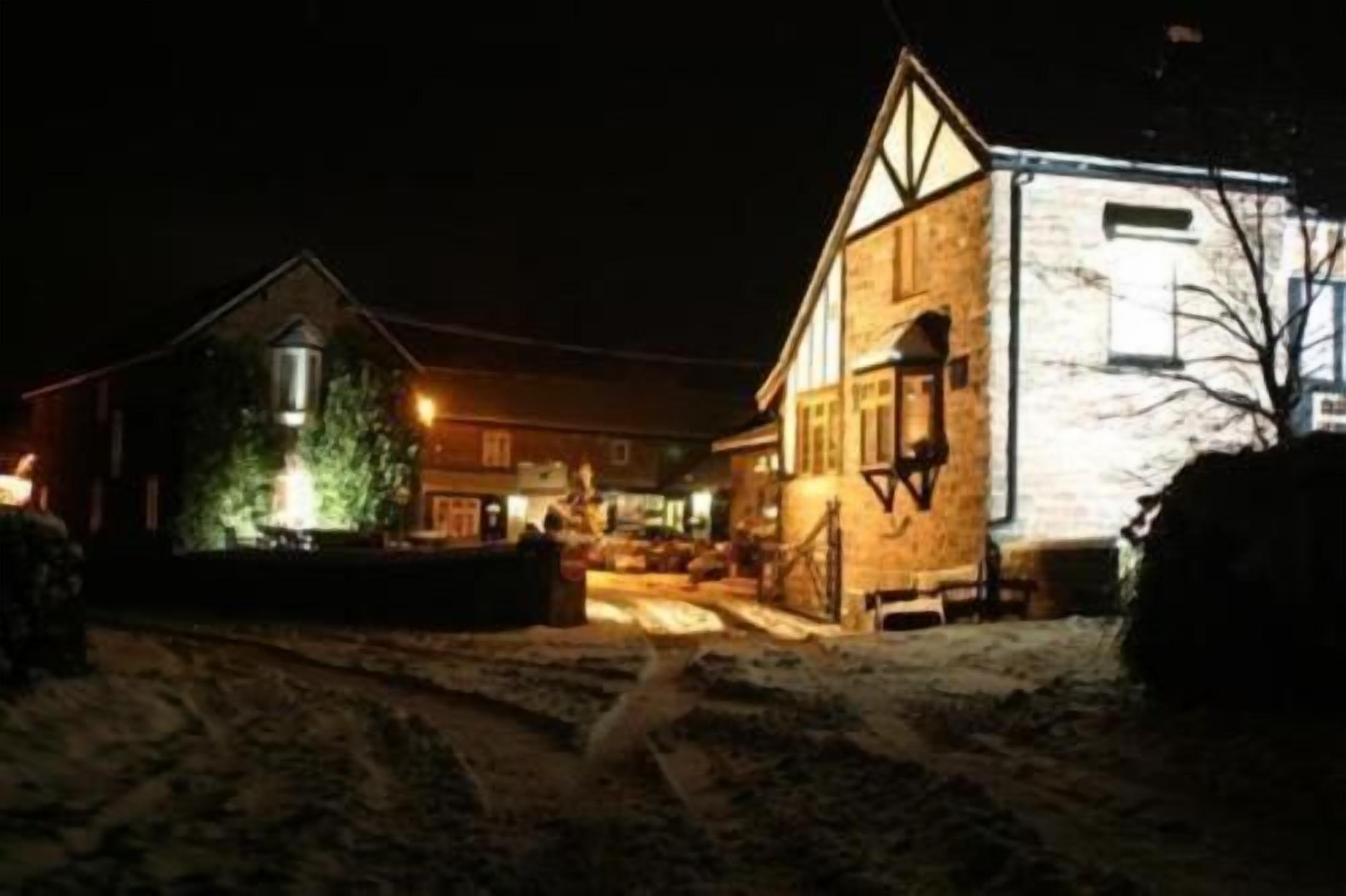 Une rue enneigée de nuit, avec un bâtiment doté d’une grande fenêtre et d’une enseigne illuminée.
