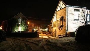 Une rue enneigée de nuit, avec un bâtiment doté d’une grande fenêtre et d’une enseigne illuminée.