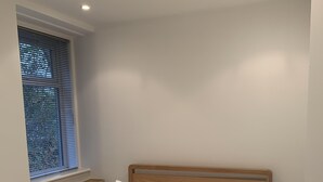 Una cama bien tendida con sábanas y almohadas blancas, un cabecero de madera y una mesita de noche con una lámpara.