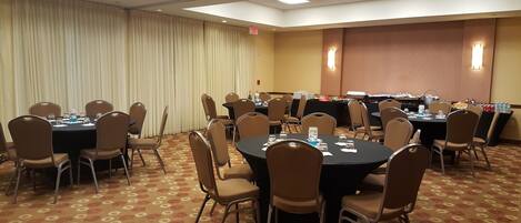 A conference room with round tables and chairs, a projector, and a buffet table with food and drinks.