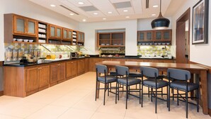 A modern kitchen with wooden cabinets, a central island with bar stools, and a large pendant light. - Hyatt Place Sarasota/Bradenton Airport (Sarasota)