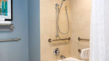 A bathroom with a bathtub, shower, and handrails.