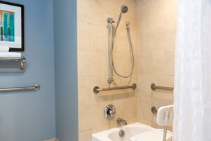 A bathroom with a bathtub, shower, and handrails.