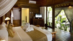 Quarto de madeira com cama, televisão e vista para palmeiras.