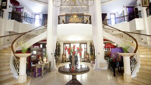Um hall imponente com uma fonte central, um lustre e uma escadaria para um andar superior.