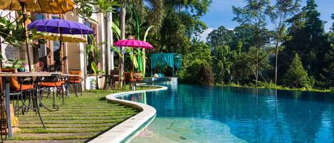 A swimming pool with a curved edge, surrounded by outdoor seating and umbrellas.