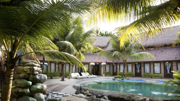 Um resort com piscina, palmeiras e um edifício com telhado de palha.